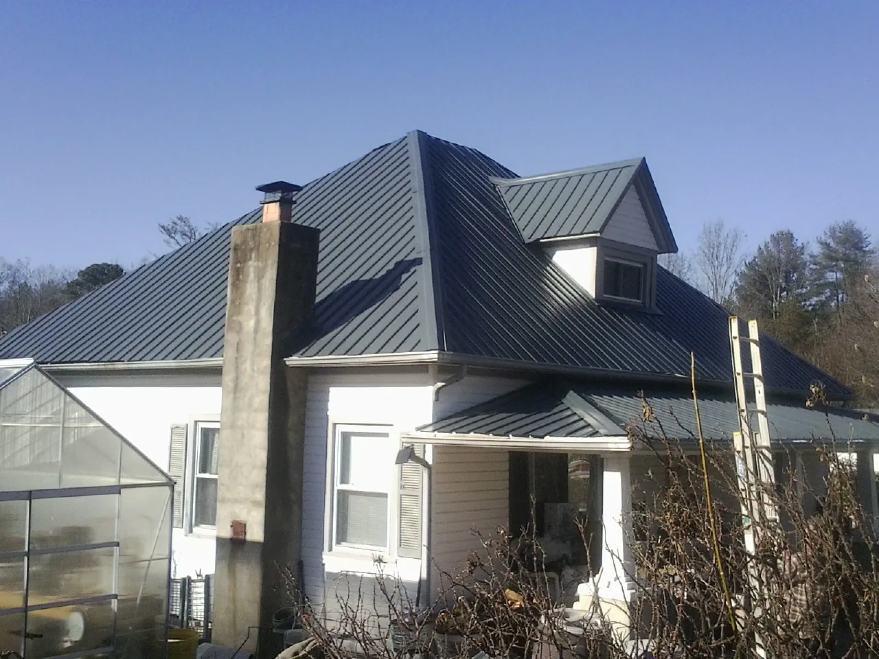 Dark blue standing seam metal roof on a white farmhouse with dormer — Slate & Tile Roof Repair by Roofing Brothers in East Texas