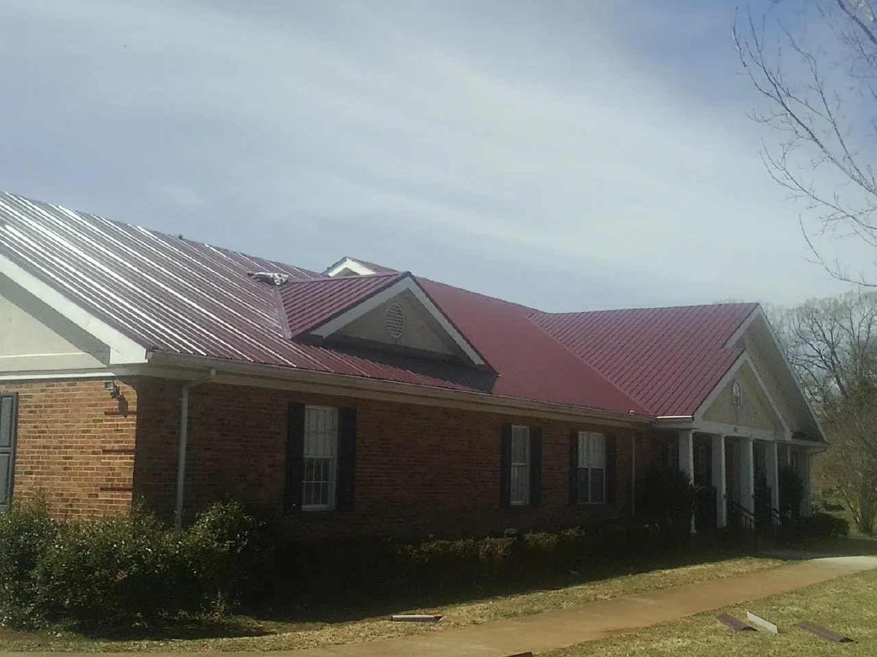 Red metal roof with gabled entries on a long brick building, from a Hail Damage Roof Repair job in East Texas