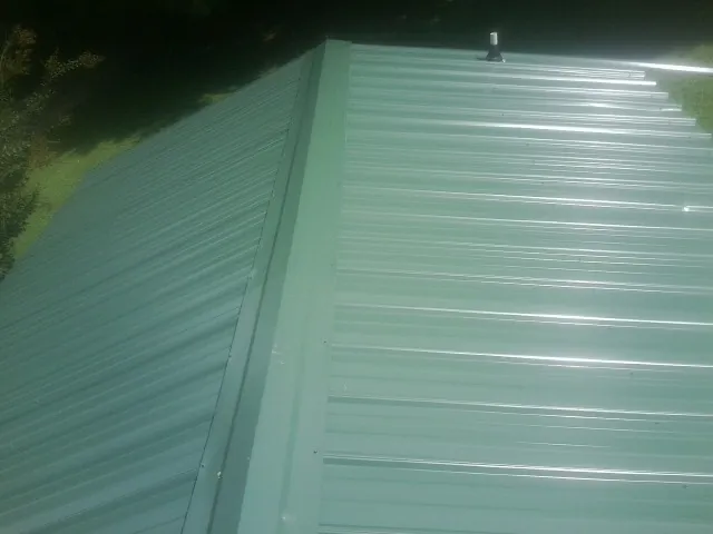New green metal panels meeting at the ridge of a roof — Flat Roof Repair work by our crew in East Texas