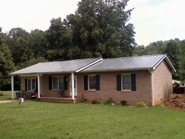 Gray metal roof on a brick ranch house with a side carport in East Texas