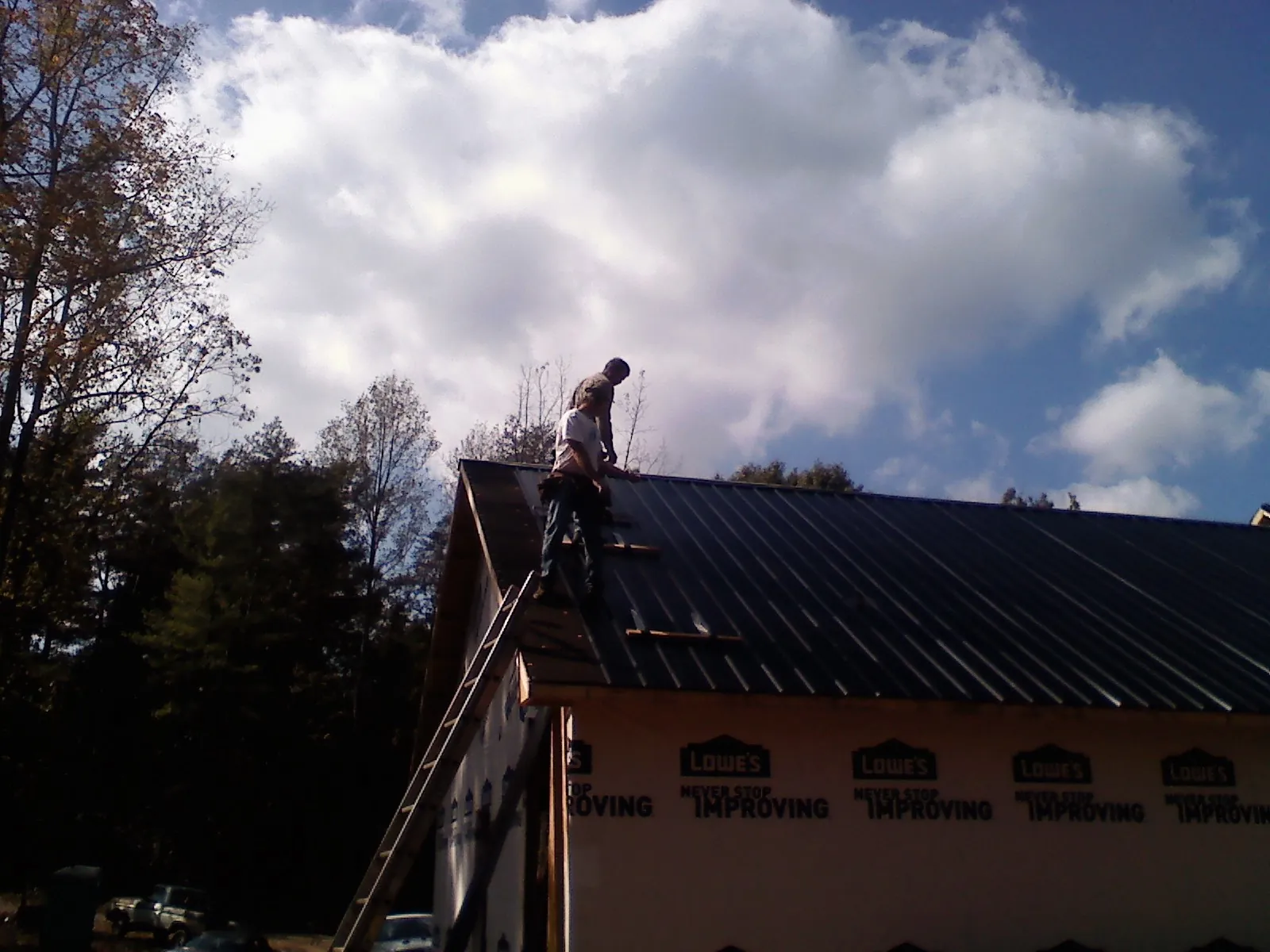Roofer fastening dark metal panels high against a cloudy sky, from a Roof Inspection job in East Texas
