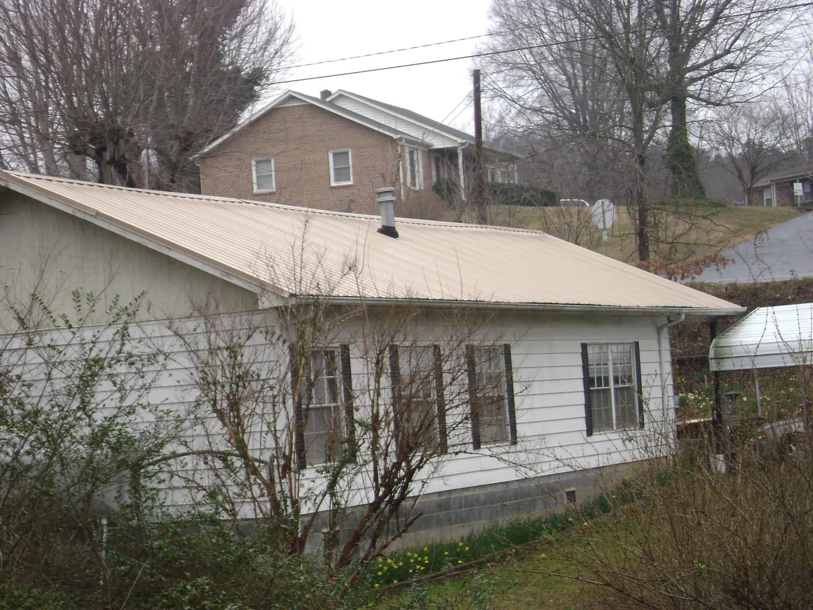 Tan metal roof on a white sided house set into a hillside — Commercial Roofing by Roofing Brothers in East Texas