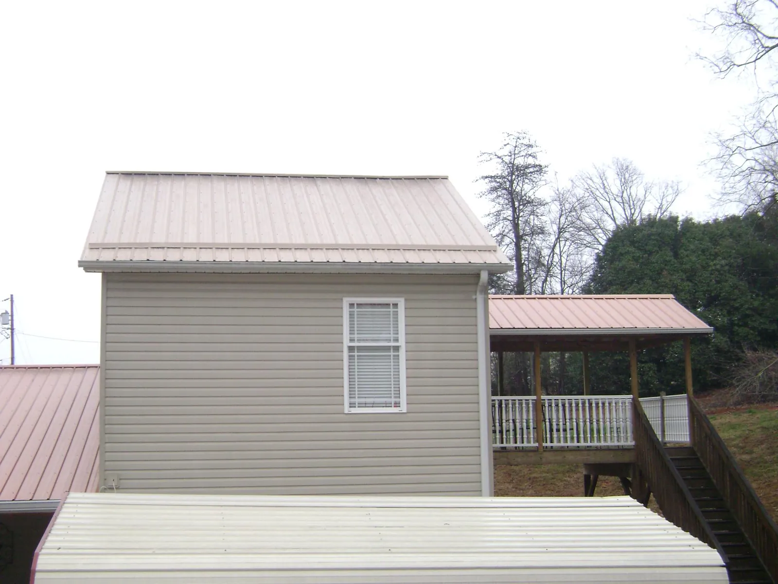 Tan metal roofs on a two story addition and attached porch, from a Roof Replacement job in East Texas